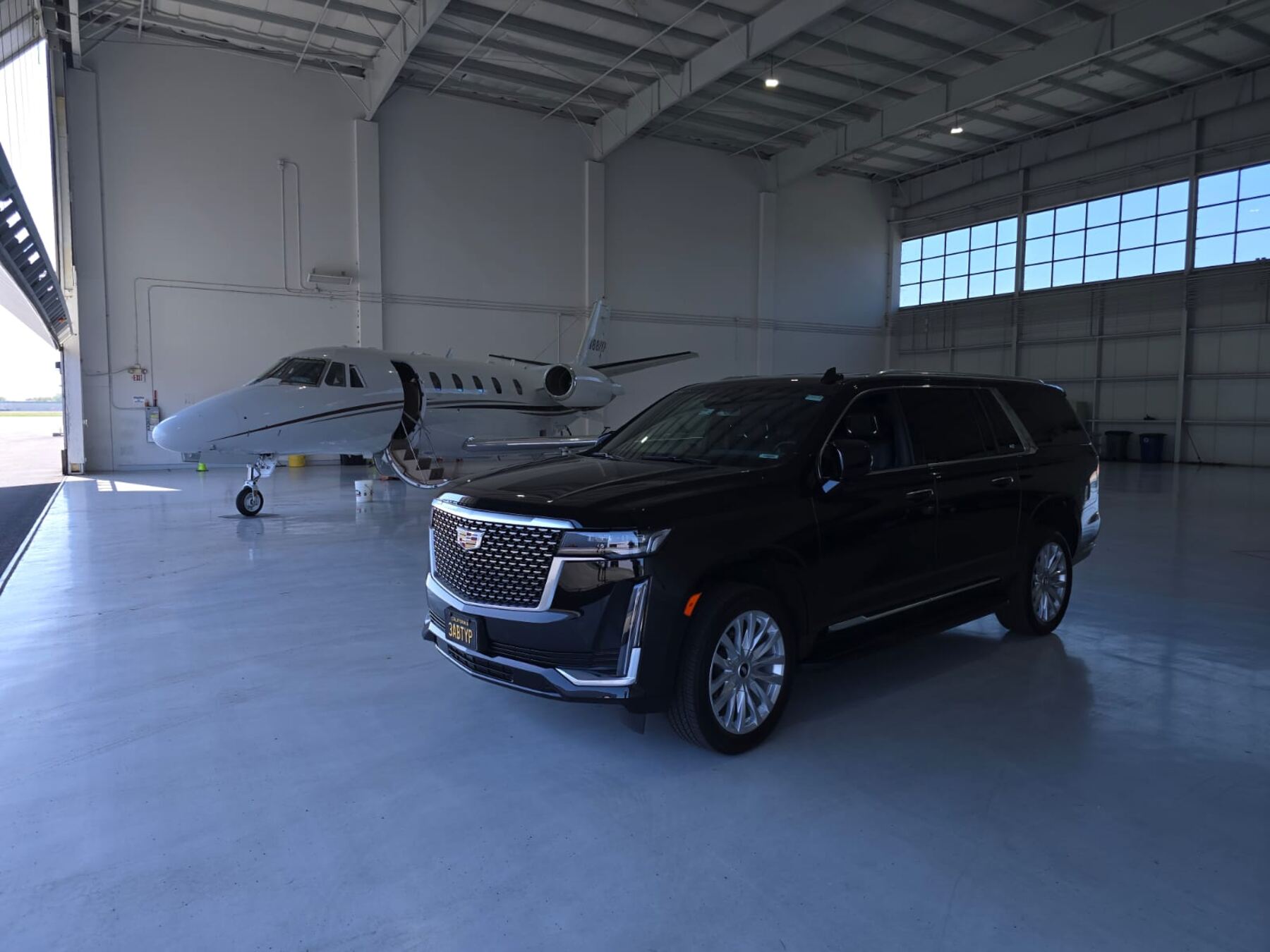SFDRIVEN Cadillac Escalade parked beside a private jet in an FBO hangar